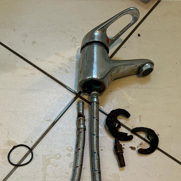 Broken tap disassembled with parts laid out on tiles